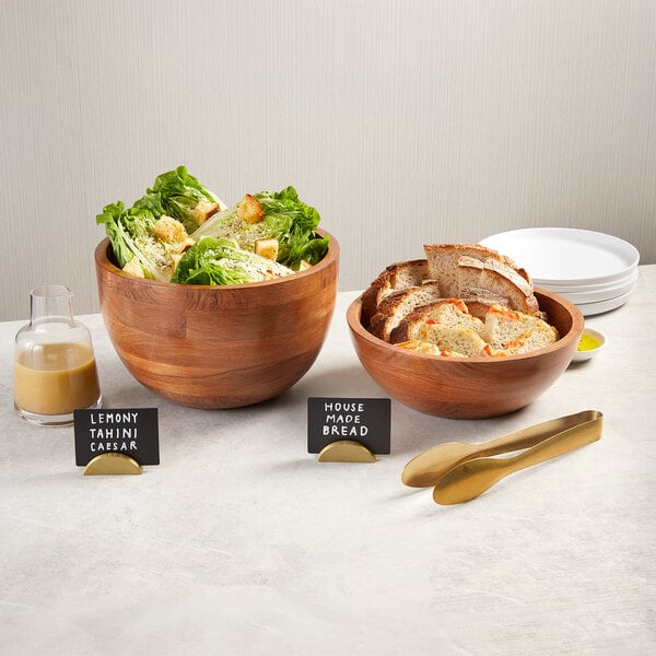 A set of round acacia wood hourglass bowls, one filled with salad and the other with sliced bread.