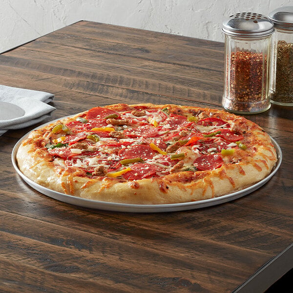 An 18-inch aluminum tapered stackable pizza pan holding a cooked pizza with various toppings.