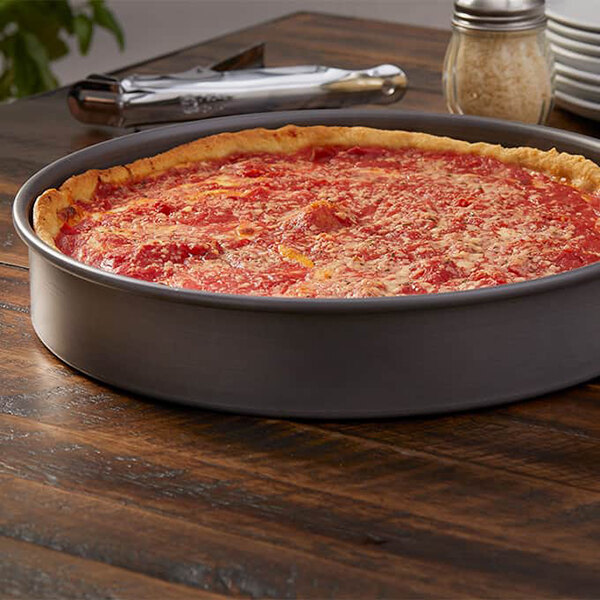 A round, straight-sided aluminum pizza pan containing a deep-dish pizza.