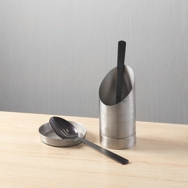 An etched stainless steel upright spoon rest with a matching base and a black-handled spoon.