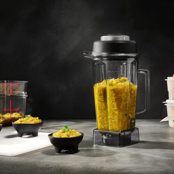 A Vitamix POWER-PREP 2.7 hp blender with a 1.5 gallon Big Batch container and a 64 oz. culinary container, shown filled with blended food.