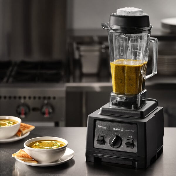 A Vitamix POWER-PREP 2.7 hp blender with a 64 oz. culinary container, shown on a kitchen counter with soup inside.