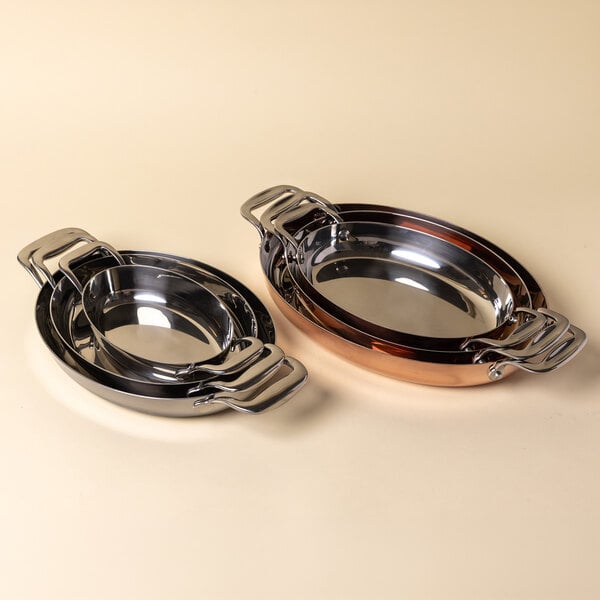 A set of stainless steel oval roasting pans with handles, shown in nested stacks.