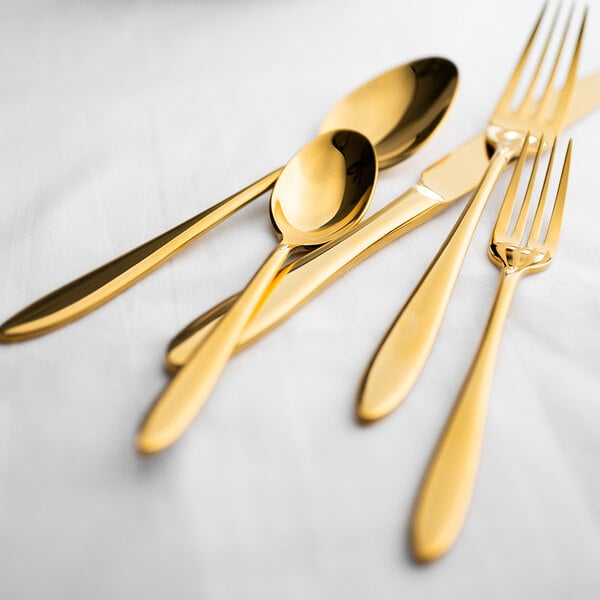 A set of gold-colored stainless steel flatware including a dinner knife, forks, and spoons displayed on a white surface.