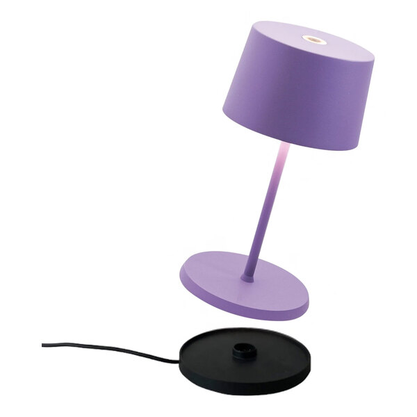 A small lilac cordless rechargeable table lamp with a matching base and a separate black charging pad.