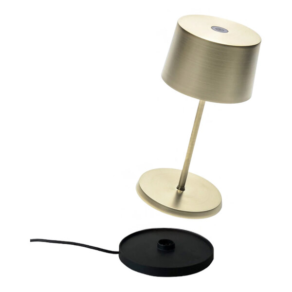 A satin brass cordless rechargeable table lamp with a matching base and a separate black charging pad.