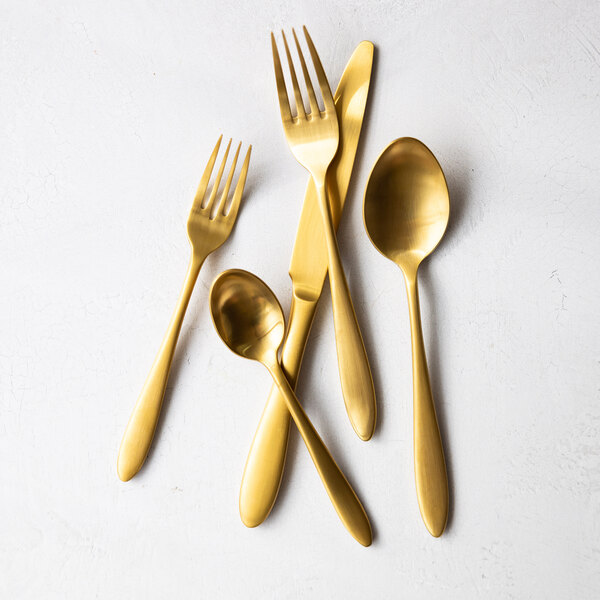 A set of matte gold stainless steel flatware including forks, spoons, and a knife.