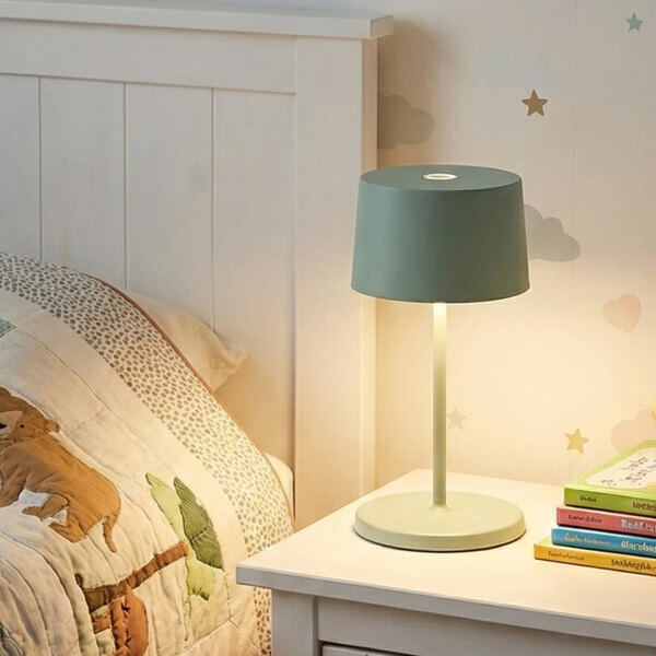 A small sage green cordless rechargeable table lamp on a bedside table.