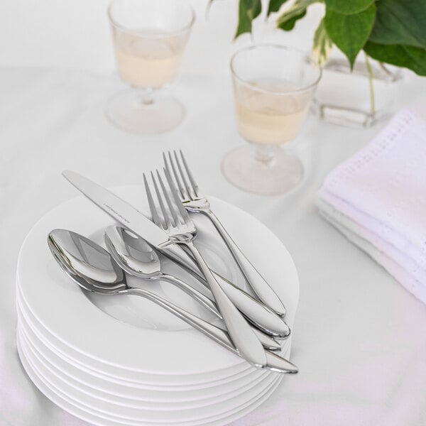A set of stainless steel dinner forks, spoons, and a knife placed on a stack of white plates on a table.