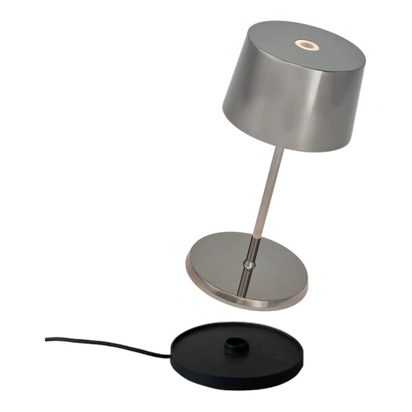 A small cordless rechargeable table lamp in antique nickel finish with a round base and a separate charging pad.