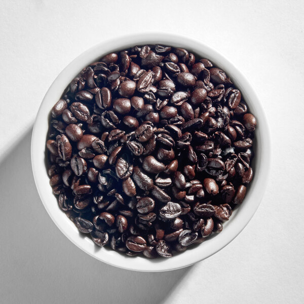 A white bowl filled with dark roasted whole coffee beans.