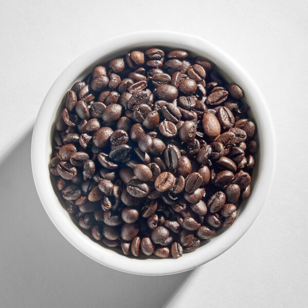 A white bowl filled with dark roasted whole coffee beans.