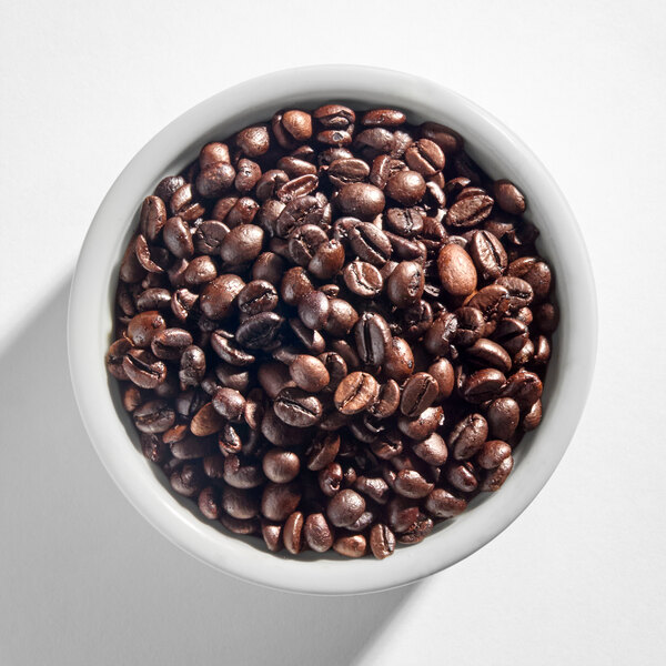 A white bowl filled with dark roasted whole coffee beans.