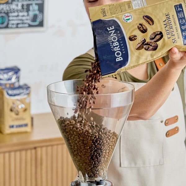 A person pours Caffe Borbone Crema Superiore whole bean espresso from a 2.2 lb. bag into a large coffee grinder hopper.