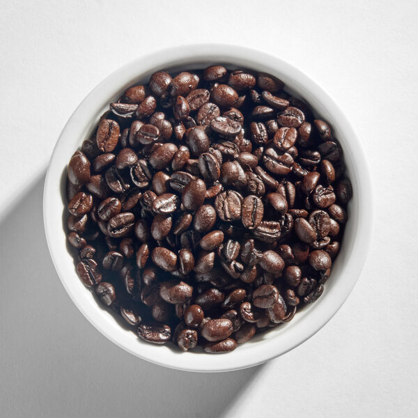 A white bowl filled with dark roasted whole coffee beans.