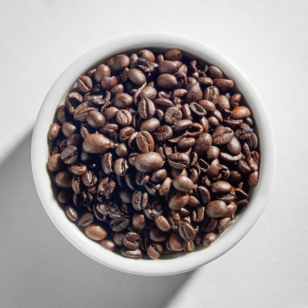 A white bowl filled with dark roasted whole coffee beans.