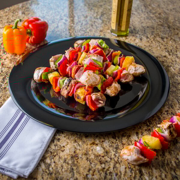 A Carlisle black melamine platter with skewers of peppers and onions on a table.