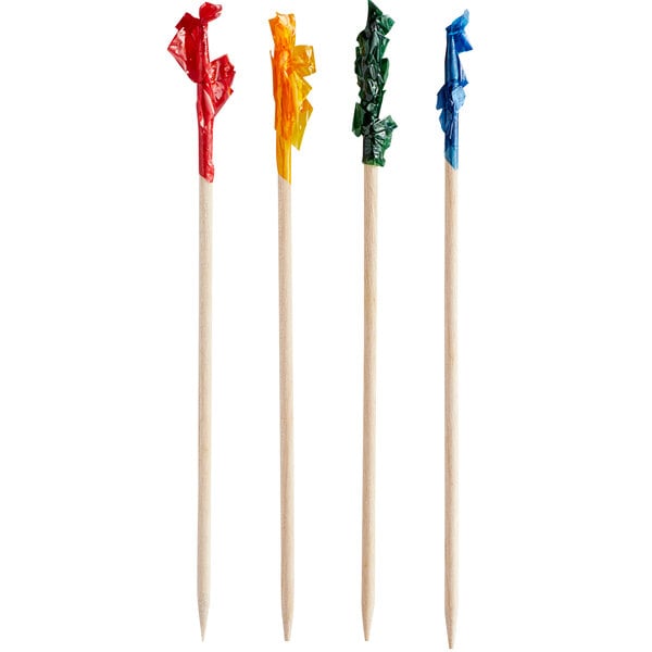 Four wooden food picks with pointed ends, each topped with a crinkled piece of colored plastic in red, yellow, green, and blue.