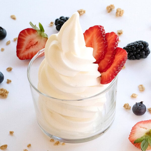 A glass cup of tart frozen yogurt topped with sliced strawberries, surrounded by assorted berries and granola pieces.