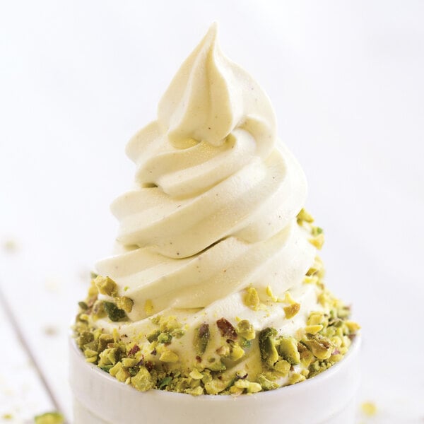 A serving of soft-serve frozen yogurt topped with chopped pistachios in a white cup.