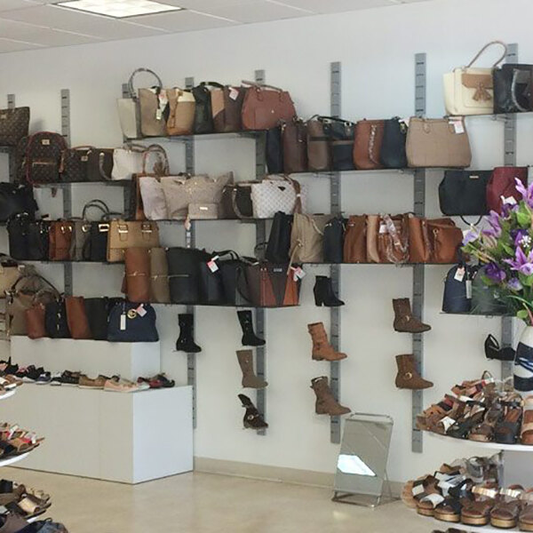 A vertical wall-mounted retail shoe and handbag display system with multiple shelves and displayers for shoes and handbags.