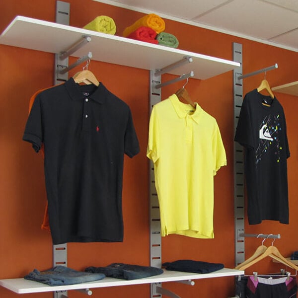 A vertical wall-mounted retail clothing display with three shirts on hangers, shelves above and below, and folded clothes on the lower shelf.