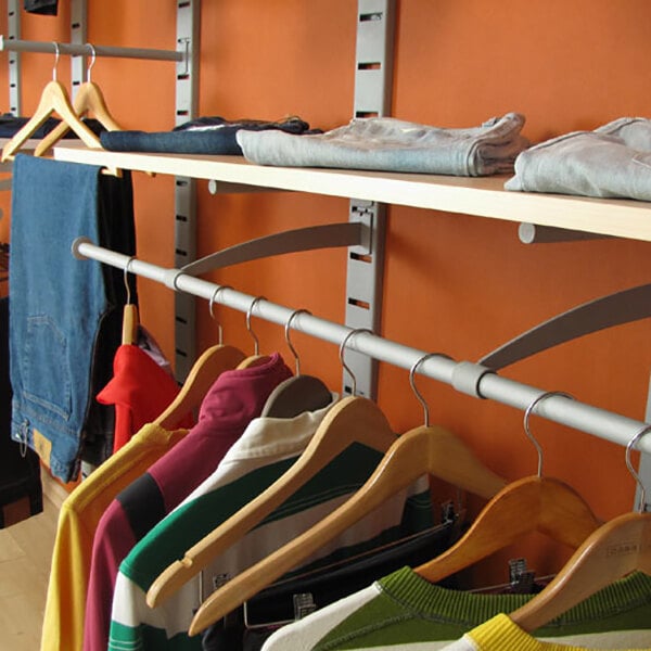 A vertical wall-mounted retail clothing display system with shelves, hanging rail, and faceouts for organizing clothes.