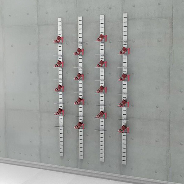 A vertical wall-mounted retail shoe display system with multiple metal slat strips and red plate-type shoe holders arranged in three sections.