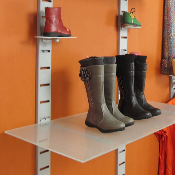 A vertical wall-mount retail display with slat strips and glass shelves showcasing various pairs of boots and shoes.