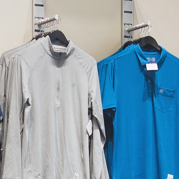 A vertical wall-mounted retail clothing display with a hanging rail and two faceouts, holding shirts on hangers.