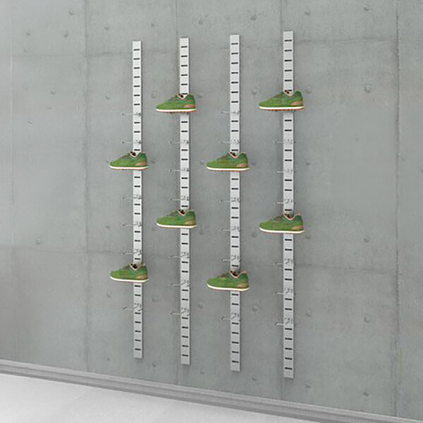 A vertical wall-mounted retail shoe display with multiple metal slat strips and green shoes showcased on individual holders.