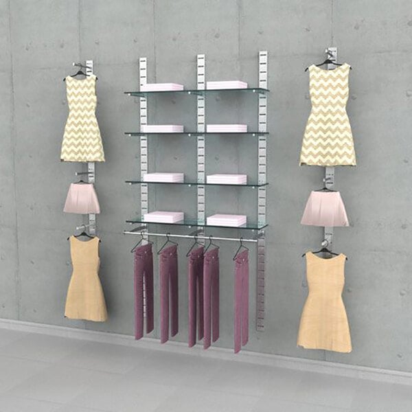 A vertical wall-mounted retail clothing display system with multiple glass shelves, hanging rails, and faceouts for showcasing dresses, skirts, and folded garments.