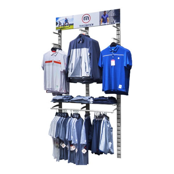 A vertical wall-mounted retail clothing display with hanging rails, faceouts, and shelves holding various shirts and jackets.