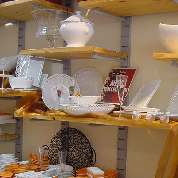 A vertical wall-mounted retail display featuring multiple wooden shelves holding various dishware and glassware items.