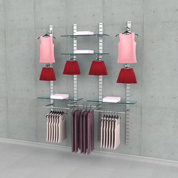 A vertical wall-mount retail clothing display system with three sections, featuring metal slat strips, glass shelves, hanging rails, and faceouts for showcasing apparel.