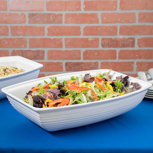 Two white Tablecraft cast aluminum salad bowls filled with salad and vegetables on a table in a salad bar.