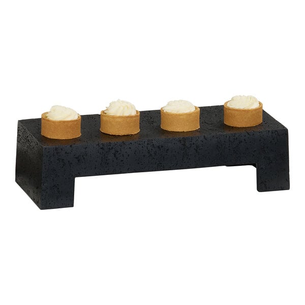 A black resin riser displaying four small round desserts with cream topping.