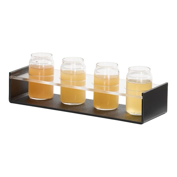 A classic black and clear caddy holding four small glasses filled with light-colored beverages.
