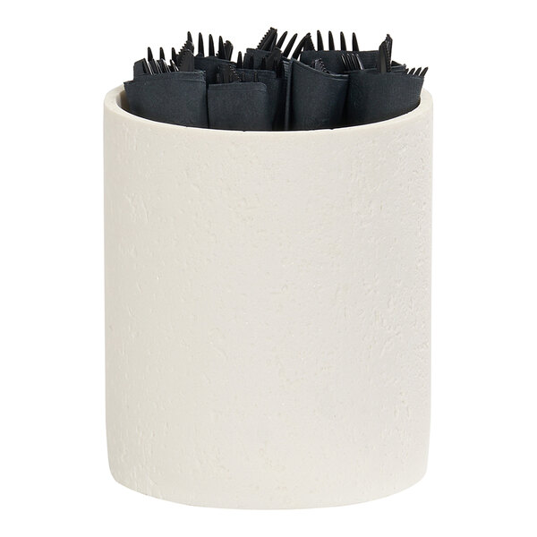 A cylindrical ivory resin riser holding black wrapped utensils.
