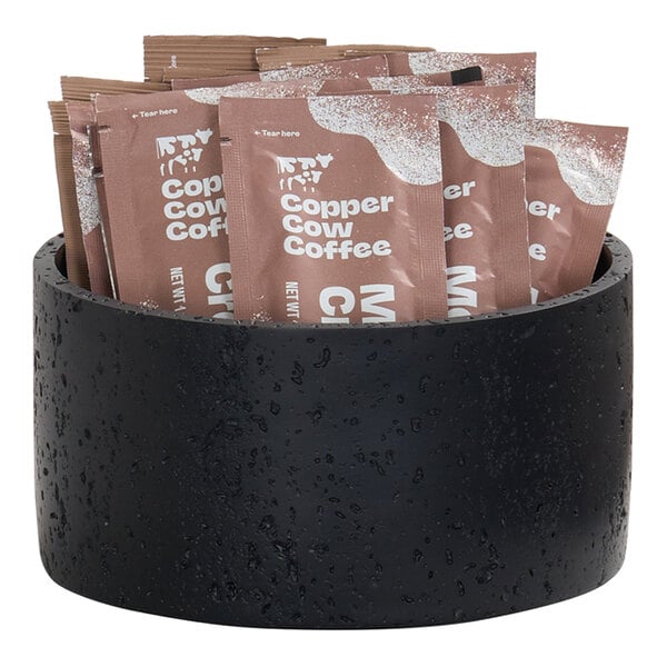 A black resin riser holding several packets of Copper Cow Coffee.