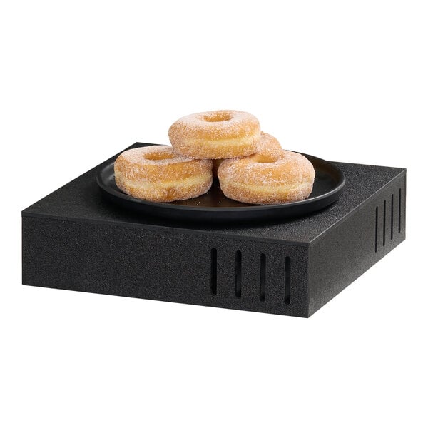 A black square riser measuring 12x12x3 inches with a plate of sugar-coated donuts on top.