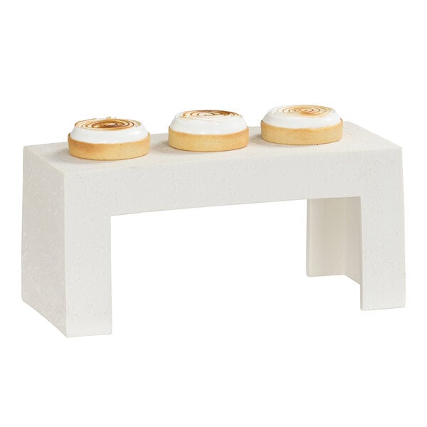 A rectangular ivory resin riser with three round pastries displayed on top.