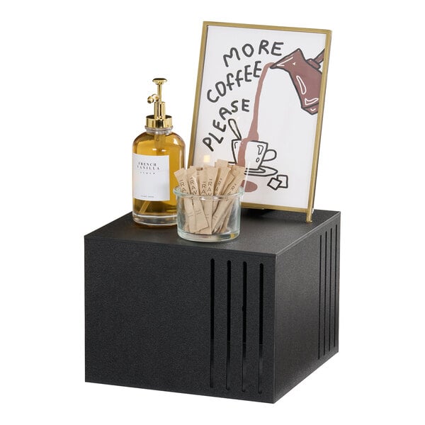 A black classic square riser measuring 12x12x9 inches, displayed with a framed sign, a glass dispenser, and a glass container with packets on top.
