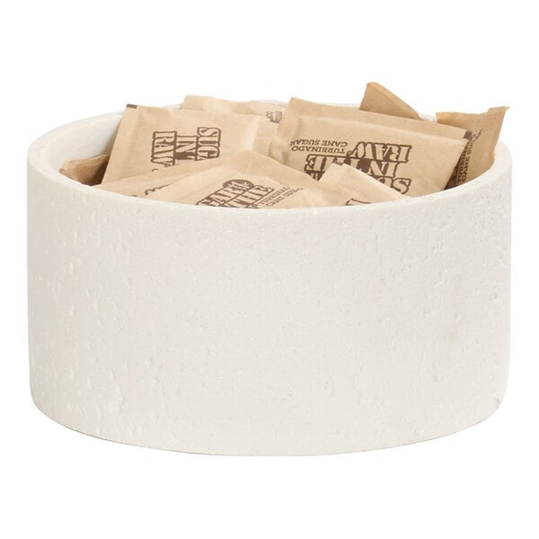A round ivory resin riser holding several packets of sugar.
