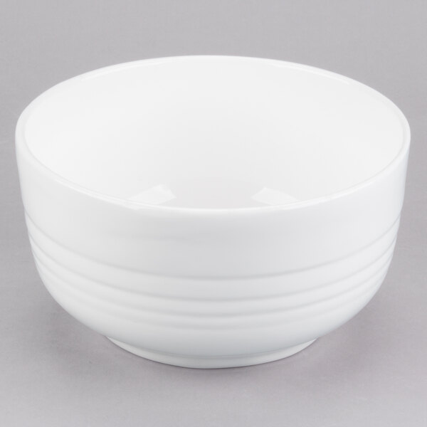 A white Tablecraft cast aluminum fruit bowl with a white rim on a gray surface.