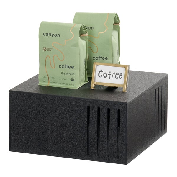 A black square display riser with two bags of coffee and a small sign labeled 'Coffee' on top.