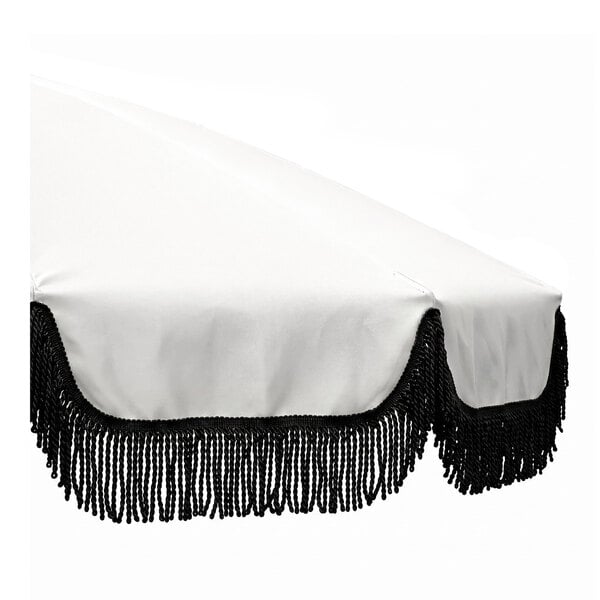 An outdoor umbrella with a natural-colored canopy, black fringe trim, and a black aluminum pole.