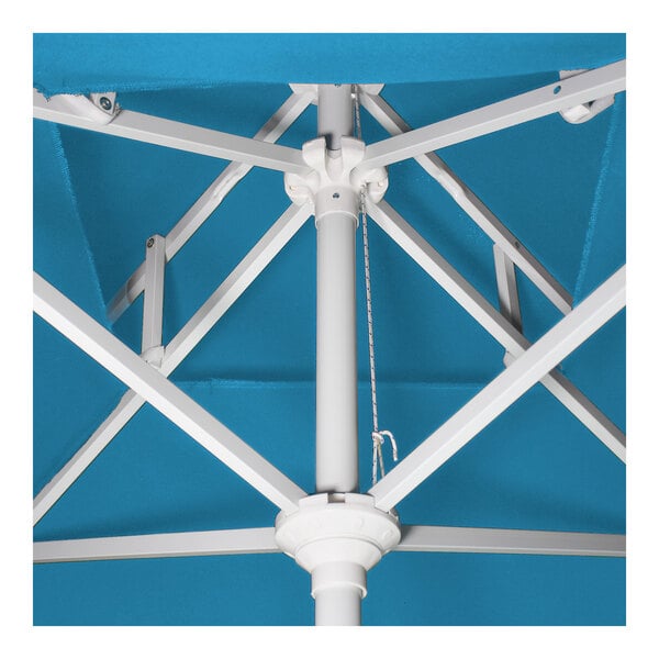 A close-up view of the internal frame and pole of a cyan round patio umbrella with a white aluminum structure.