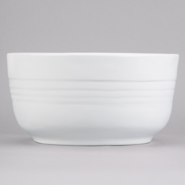 A white Tablecraft cast aluminum fruit bowl with a white rim on a gray background.