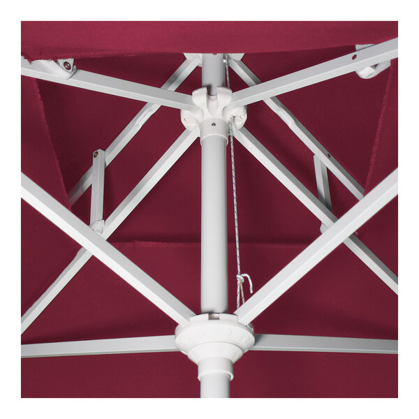 A close-up view of the white aluminum frame and crank mechanism of a hot pink round patio umbrella.